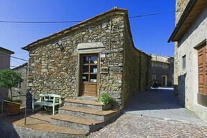 Um edifício de pedra com uma porta de madeira, degraus que levam à entrada e um banco na parte externa.