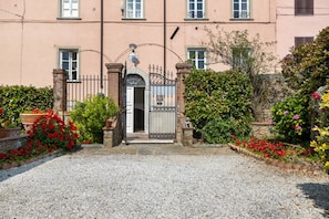 Um edifício com entrada protegida por portão, um caminho de acesso de cascalho e um jardim com flores vermelhas.