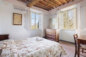 Ein Schlafzimmer mit Bett, Kommode und einem Fenster mit Blick auf Bäume.
