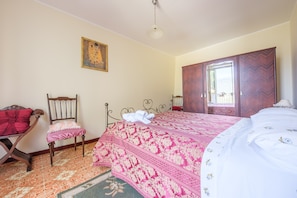 Un dormitorio con una cama, una silla, un armario y un cuadro en la pared.
