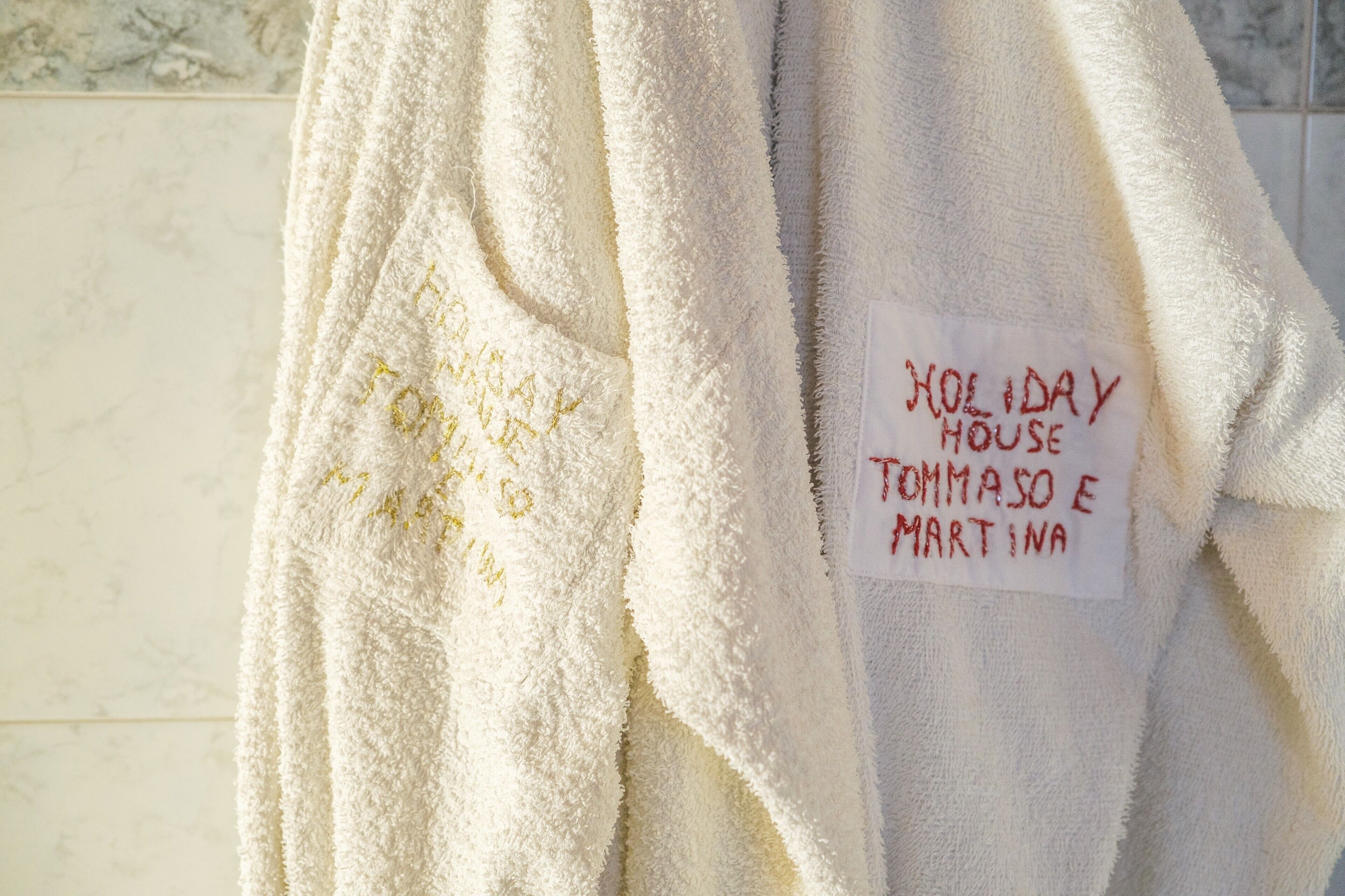 Toalha branca com a inscrição 'HOLIDAY HOUSE TOMMASO E MARTINA' bordada.