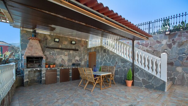 Une terrasse extérieure avec un mur en pierre, une table en bois avec des chaises, un barbecue et un escalier doté d’une rampe.