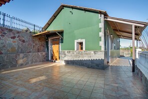 Ein Gebäude mit grüner Fassade, einer Steinwand, einer gefliesten Terrasse und einem Metallzaun.