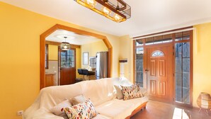 Un salon avec un canapé, une porte en bois et un coin cuisine visible à travers une arche.