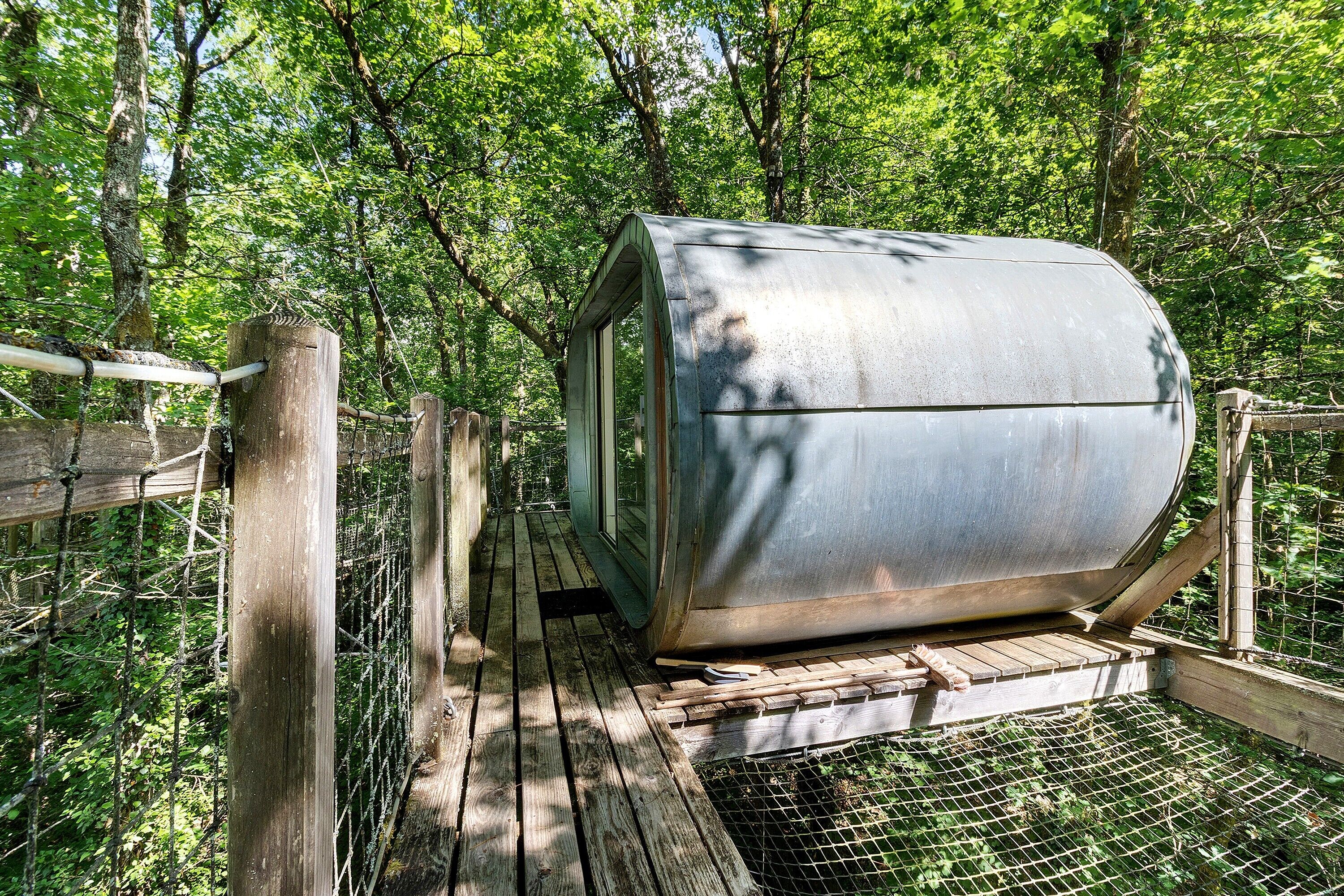 Eine rustikale Holzhütte mit Metalldach, auf einer Holzterrasse gelegen, umgeben von einem Drahtzaun, inmitten eines bewaldeten Gebiets.