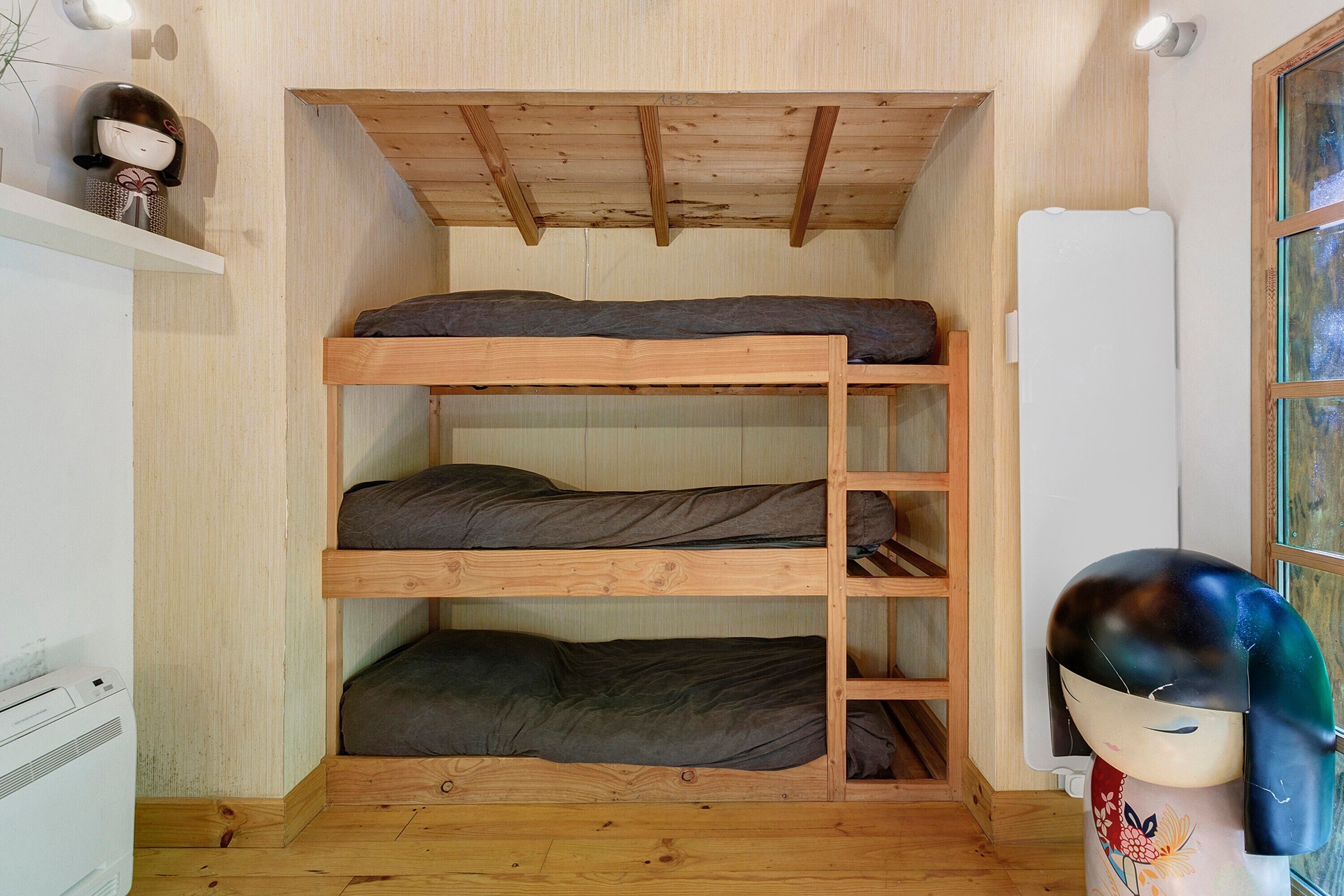 A bunk bed with three levels, wooden walls, a white radiator, and a decorative item on the left.