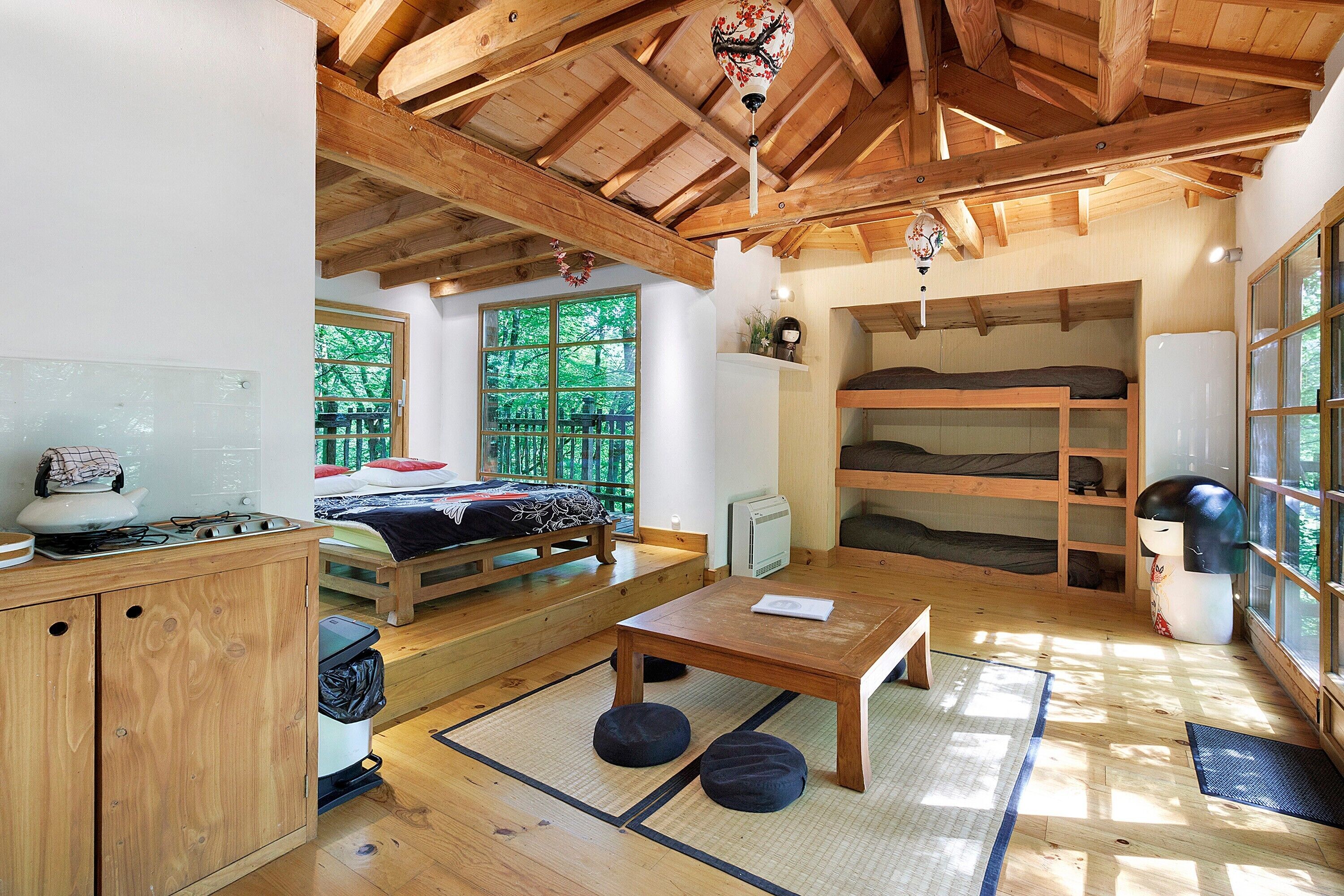 Une pièce de style japonais traditionnel, avec un sol recouvert de tatamis, une petite table en bois, un lit superposé et un coin cuisine équipé d’une cuisinière.