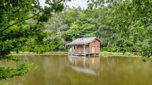 A wooden cabin by a calm lake surrounded by dense trees.