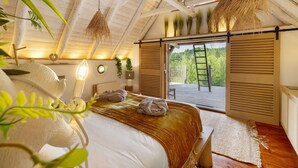 A bedroom with a bed, a window, a door, and a view of greenery.