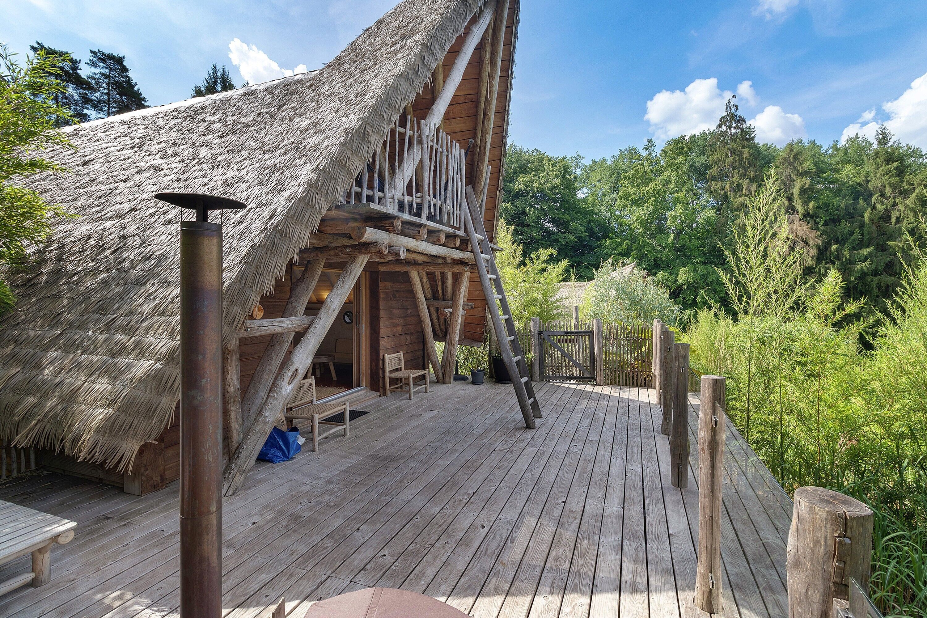 A wooden structure with a thatched roof, a wooden deck, and a staircase leading to an upper level.