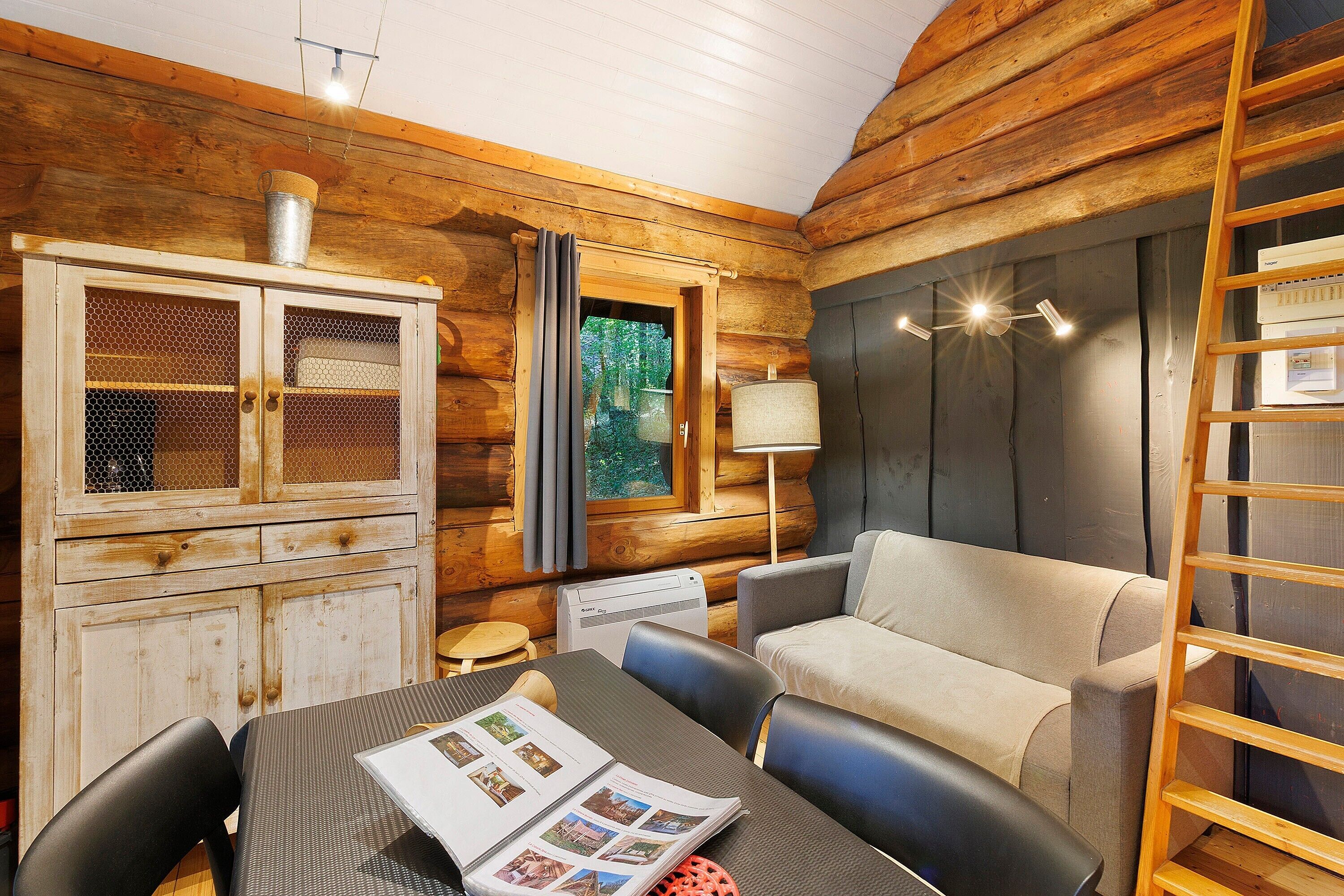 A cozy log cabin interior with a wooden cabinet, a table with a magazine, a sofa, and a ladder.