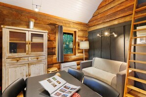 Interior acogedor de una cabaña de madera con un armario, una mesa con una revista, un sofá y una escalera.