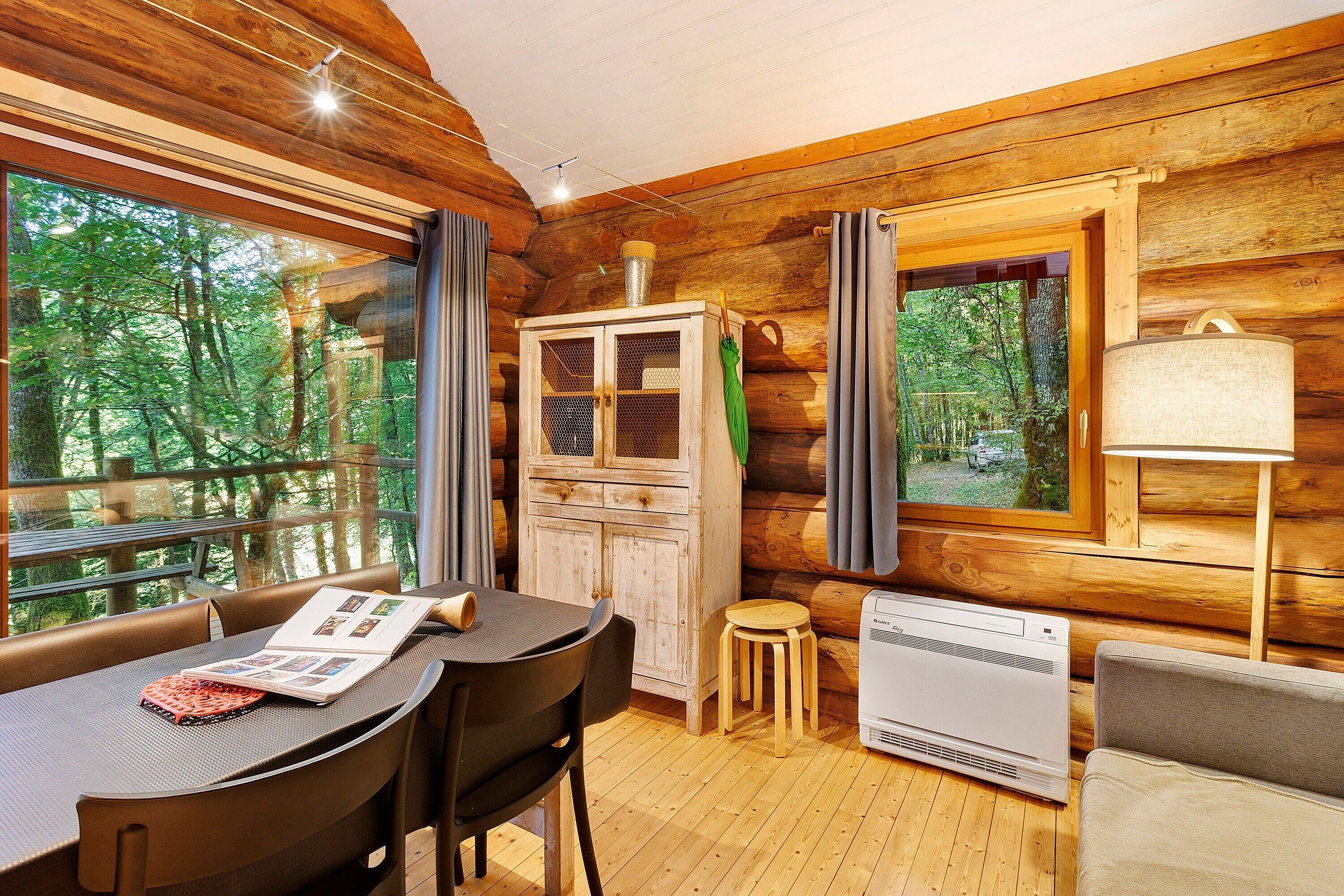 L’intérieur chaleureux d’un chalet comprend une table à manger, des chaises, un buffet, un radiateur et de grandes fenêtres donnant sur la forêt.