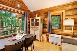 L’intérieur chaleureux d’un chalet comprend une table à manger, des chaises, un buffet, un radiateur et de grandes fenêtres donnant sur la forêt.