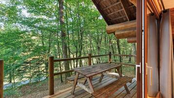 Une terrasse en bois avec une table de pique-nique, entourée d’une balustrade en bois, donnant sur une zone boisée.
