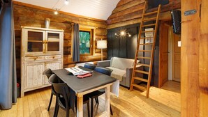 Een gezellig chaletinterieur met een eettafel, stoelen, een bank, een ladder en een kast met een gaasdeur.