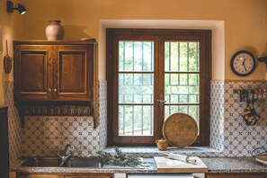 A kitchen with a window, wooden cabinets, a sink, and a clock on the wall.