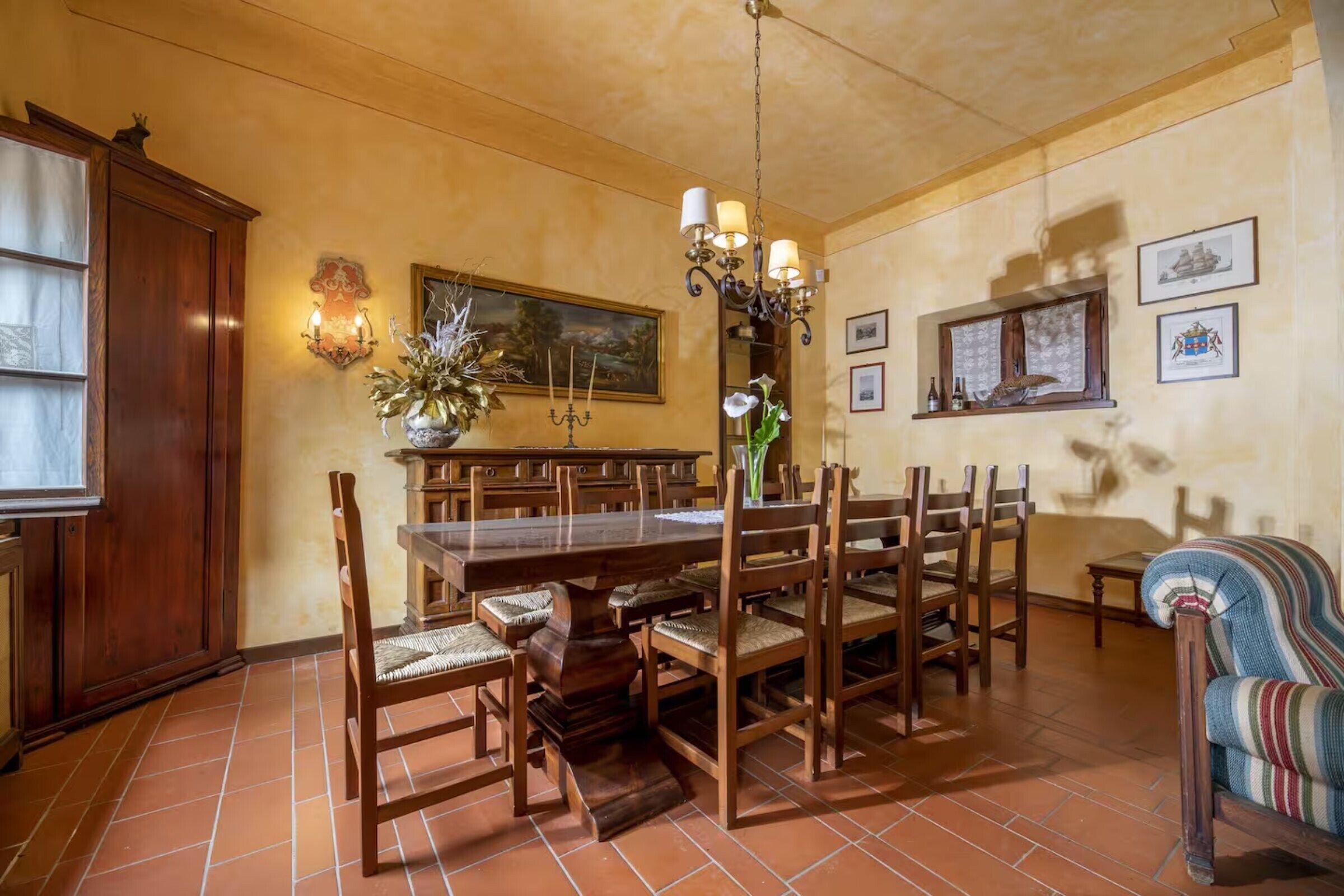Comedor con una gran mesa de madera, varias sillas, una araña y obras de arte colgadas en la pared.