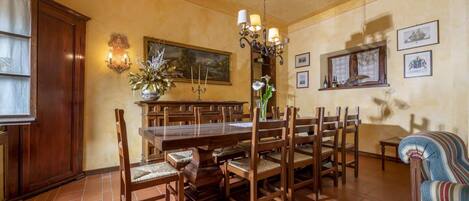 Comedor con una gran mesa de madera, varias sillas, una araña y obras de arte colgadas en la pared.