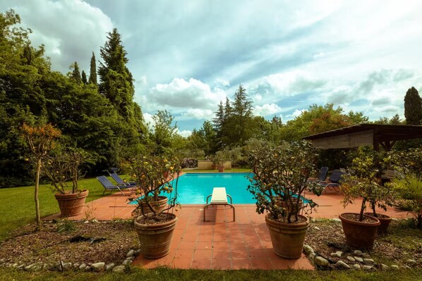 A swimming pool with lounge chairs, surrounded by potted plants and trees.