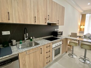 A modern kitchen with wooden cabinets, a granite countertop, a built-in oven, and a microwave. - Apartment 'Palangreros Beach' with Wi-Fi and Air Conditioning (Fuengirola)