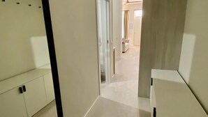 Un couloir avec un miroir, une porte et une armoire blanche.