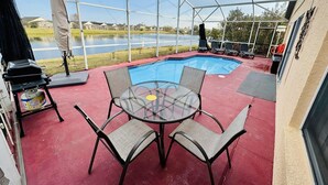 Un espacio al aire libre techado con piscina, parrilla y mesa con sillas.