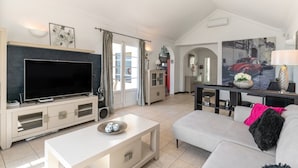 Una sala de estar moderna con un televisor de pantalla plana, un sofá, una mesa de centro y una zona de comedor con una mesa y sillas.