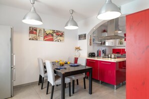 Una cocina moderna con armarios rojos, una mesa de comedor con sillas e iluminación colgante.