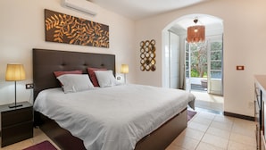 Un dormitorio con una cama grande, aire acondicionado instalado en la pared, un adorno en la pared y vistas a un área exterior a través de un arco.