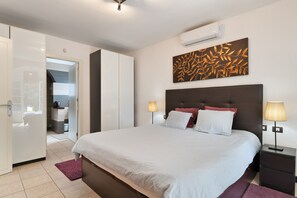 Un dormitorio con una cama grande, lámparas de noche, aire acondicionado de pared y una puerta que da a un baño.