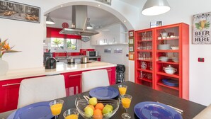 Una cocina moderna con armarios rojo y blanco, una isla central y una zona de comedor con una mesa preparada para dos.