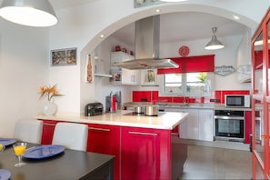 Une cuisine moderne avec des meubles de rangement rouges et blancs, un îlot central et un coin repas avec une table dressée pour deux personnes.