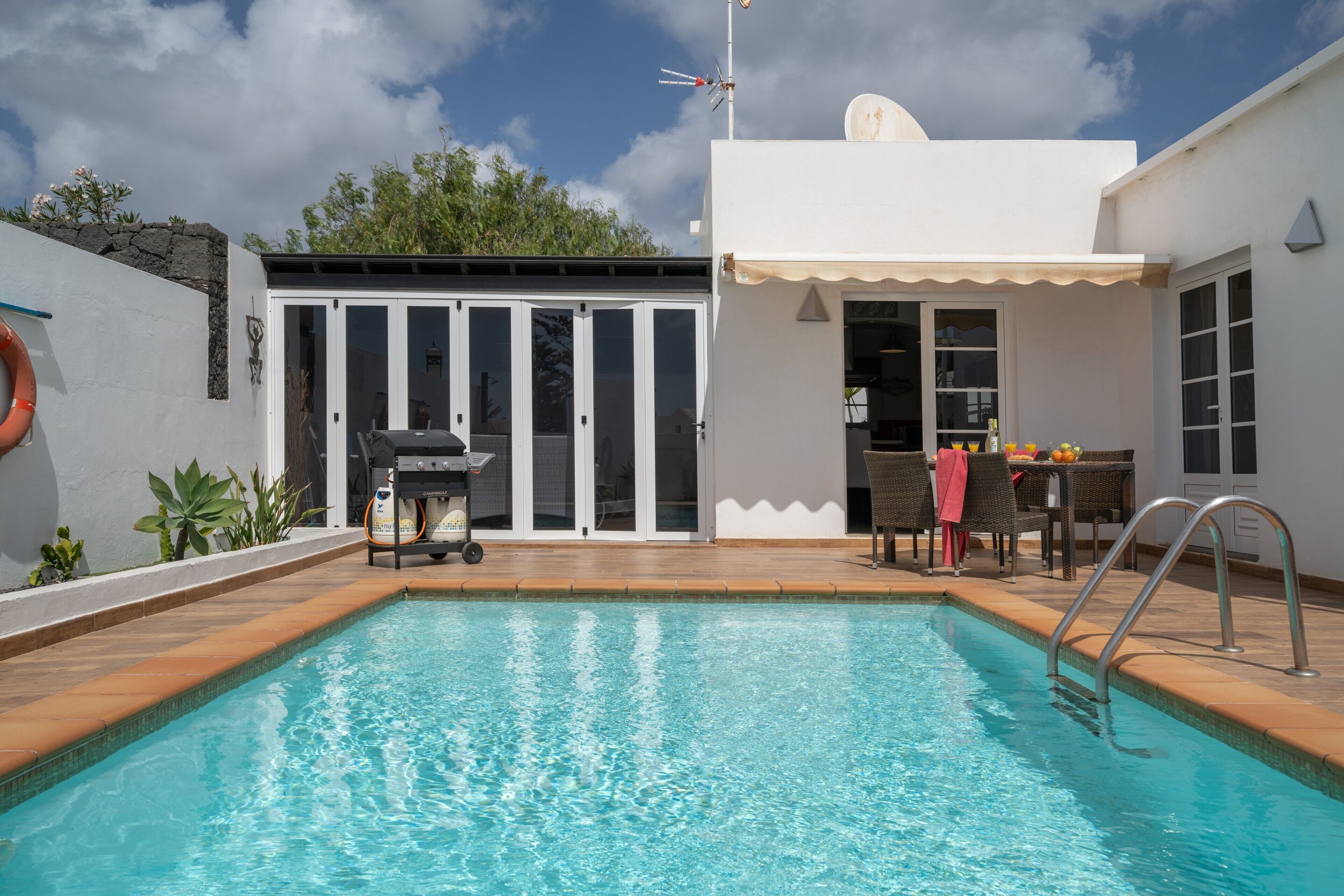 Une piscine avec un espace patio, un barbecue et un coin salon abrité.