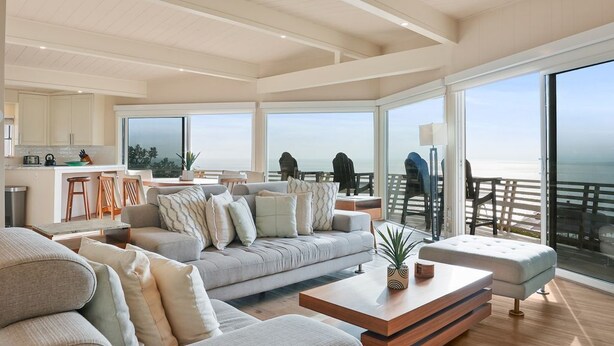 A spacious living area with a large sofa, a coffee table, and a view of the ocean through large windows. - Cliffside Oceanfront Gem - Stunning Views & Yard (Encinitas)