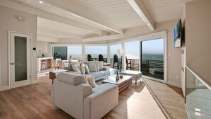 A spacious living area with a large sofa, a coffee table, and a view of the ocean through large windows. - Cliffside Oceanfront Gem - Stunning Views & Yard (Encinitas)