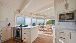 A modern kitchen with white cabinetry, a large island, and a view of the ocean. - Cliffside Oceanfront Gem - Stunning Views & Yard (Encinitas)