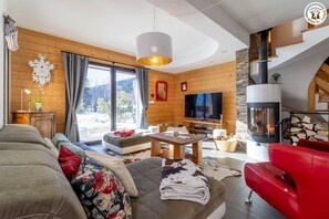 A cozy living room with a fireplace, a television, and a large window offering a view of the outdoors. - LE CHALET DU LYS - LA FECLAZ LES DESERTS (LA FECLAZ LES DESERTS)