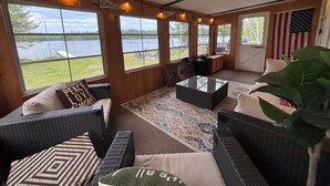 A covered outdoor seating area with wicker furniture, a coffee table, and a view of a lake.