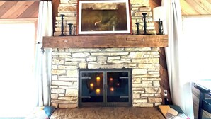 A stone fireplace with a framed picture above it, flanked by two chairs.