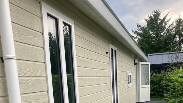 Ein Haus mit beige-farbenem Verputz, großen Schiebeglastüren und einem Schotterweg.