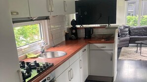 Eine kleine Küche mit weißen Schränken, einer Holz Arbeitsplatte, einem eingebauten Backofen und einem großen Fenster mit Blick auf Grünflächen.