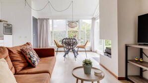 Un salon moderne comprenant un canapé, une table basse, un téléviseur posé sur un meuble et un coin repas avec une table et des chaises.