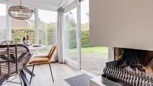Une cuisine moderne dotée d’une cuisinière intégrée, de grandes fenêtres et d’un coin repas avec des chaises en osier.