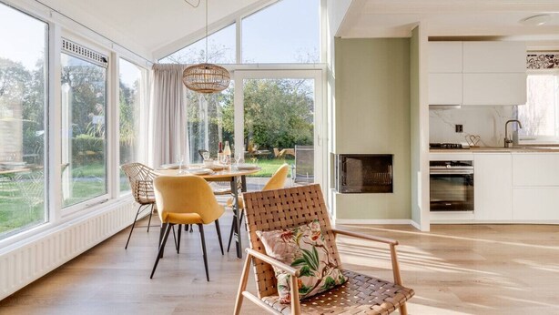 A spacious kitchen with white cabinets, a built-in oven, and a large window overlooking a garden. - Fijne gerestylede bungalow met grote zonnige tuin (Zwiggelte)