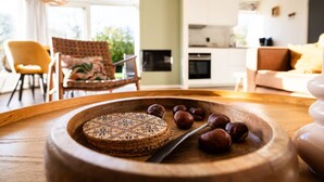 A cozy living room with a wooden table displaying a cake and hazelnuts, a yellow armchair, and a sofa. - Fijne gerestylede bungalow met grote zonnige tuin (Zwiggelte)