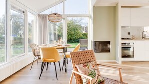 A modern kitchen with white cabinets, a built-in oven, and a dining area with yellow chairs and a table. - Fijne gerestylede bungalow met grote zonnige tuin (Zwiggelte)