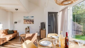 A modern living room with a dining area, a sofa, a table set for two, and a large window with curtains. - Fijne gerestylede bungalow met grote zonnige tuin (Zwiggelte)