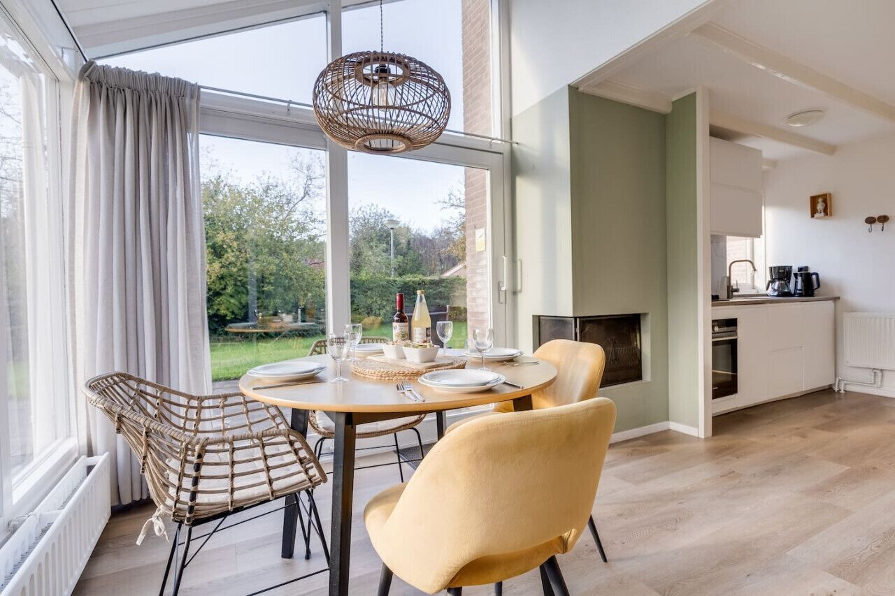 A dining area with a table set for four, a wicker chair, a yellow chair, and a hanging light fixture.