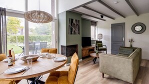 Een eetgedeelte met een ronde tafel, stoelen en een hanglamp. Achtergrond heeft een televisie en een open haard.